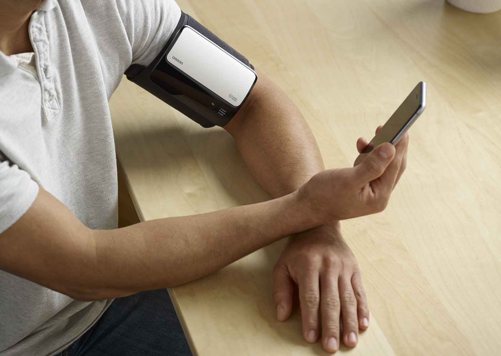 Man taking blood pressure monitor at home, looking at phone