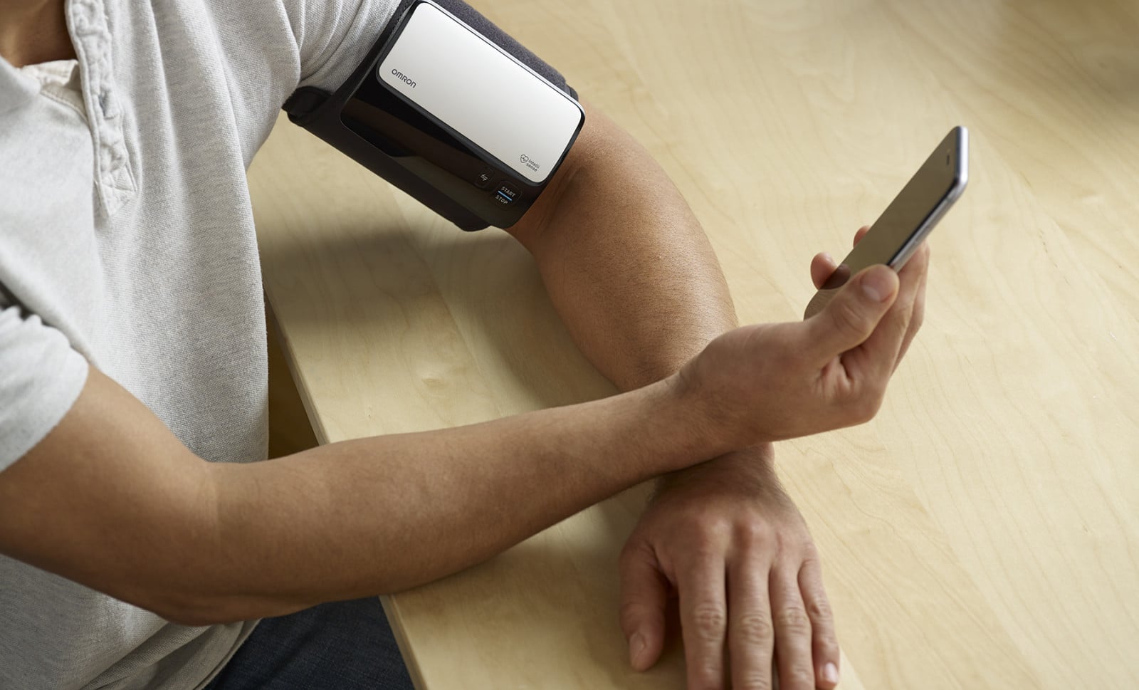Man taking blood pressure monitor at home, looking at phone
